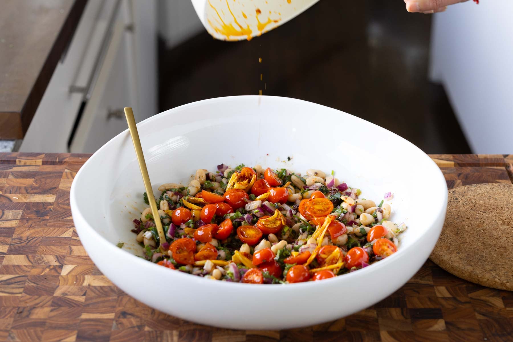 adding fried garlic and tomato to the marinated white bean salad