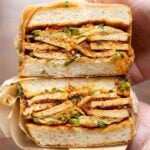 hand holding a coconut tofu sandwich wrapped in butcher paper