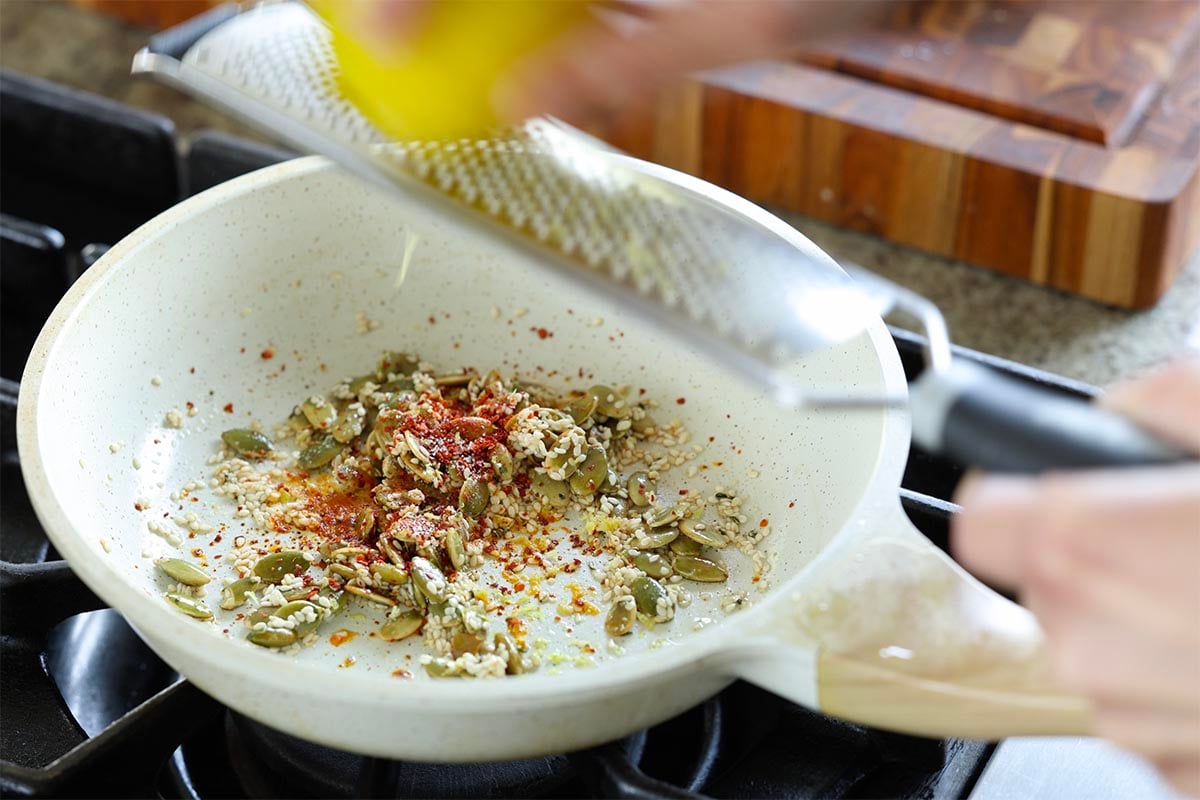 adding pepper flakes and lemon zest to the seeds in the pan