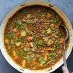 spoon serving some lentil potato soup from the pot