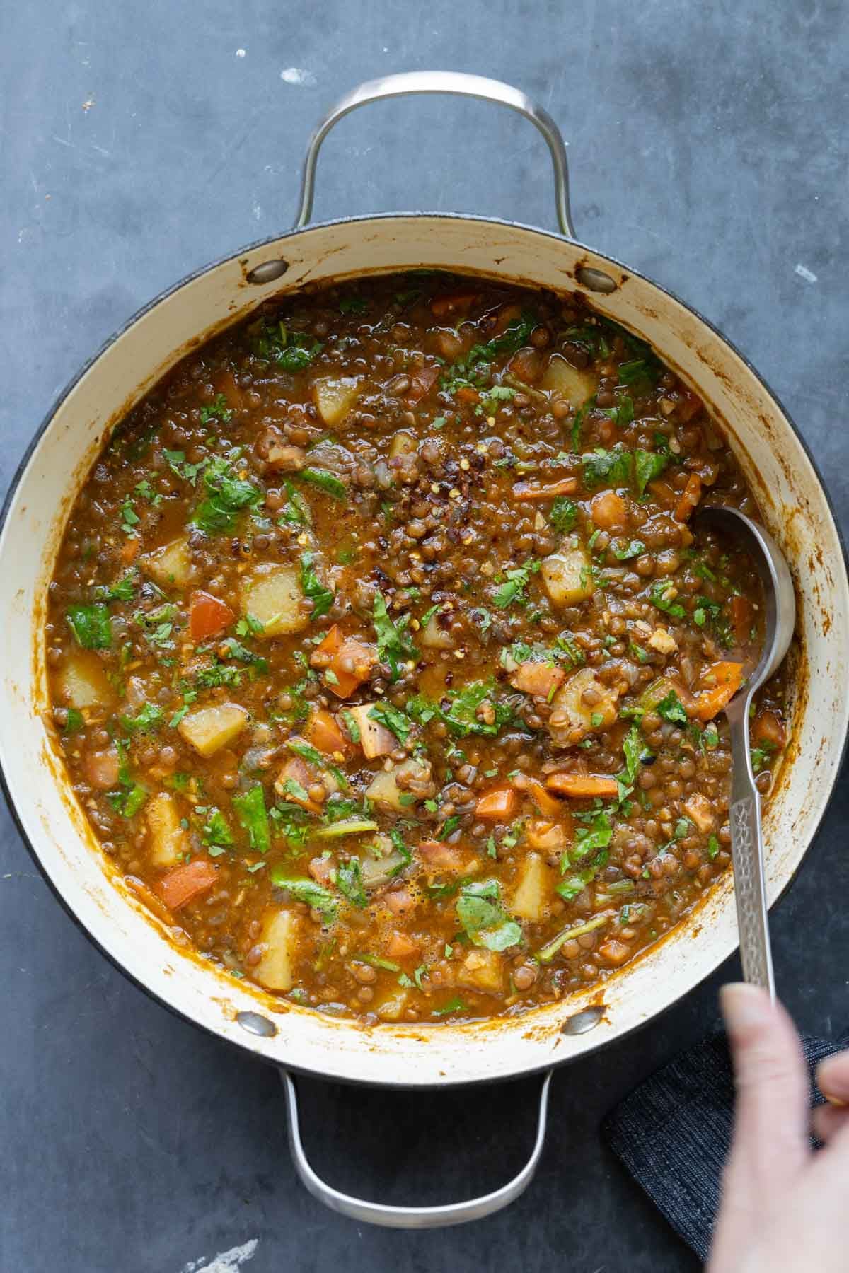 spoon serving some lentil potato soup from the pot