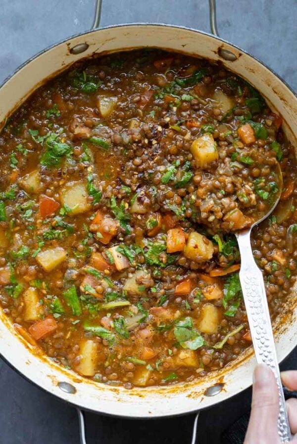 spoon serving some lentil potato soup from the pot